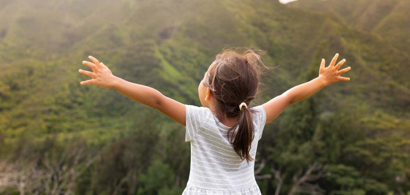 A young girl soaks in the view of Maui volcanos covered in lush tropical vegetation 